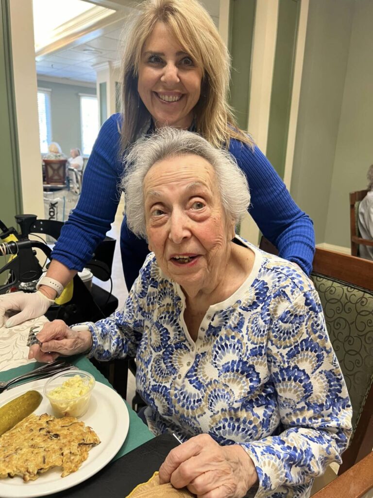 Somerset Gardens dining room with resident Somerset Gardens Assisted Living Executive Director Marla Butbul smiling with a resident in the dining room of the community in Plainview, NY in Long Island.