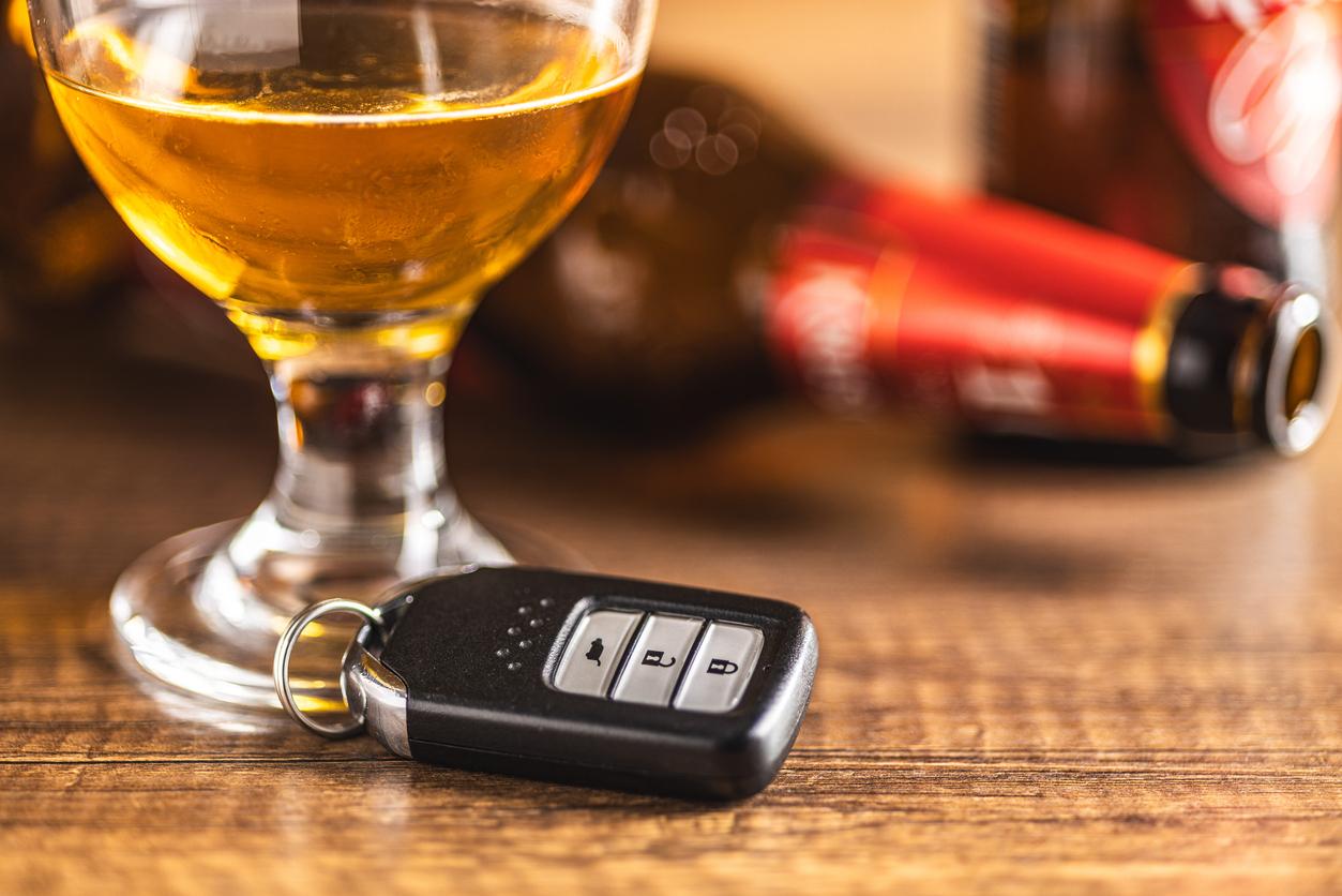 A glass of alcohol sitting beside an electronic car key and a knocked over beer bottle