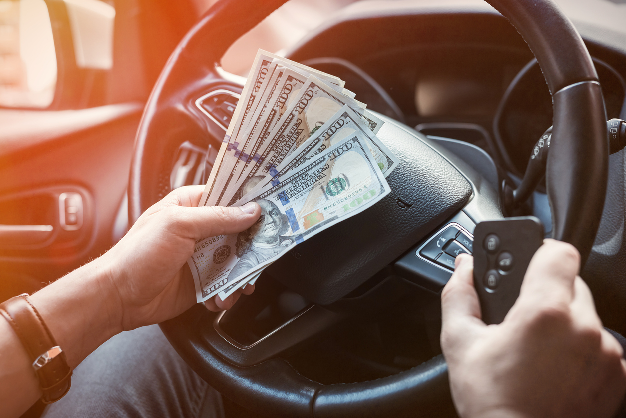 Someone behind the wheel of a car, holding a car key and cash to represent fees to renew license in Illinois.