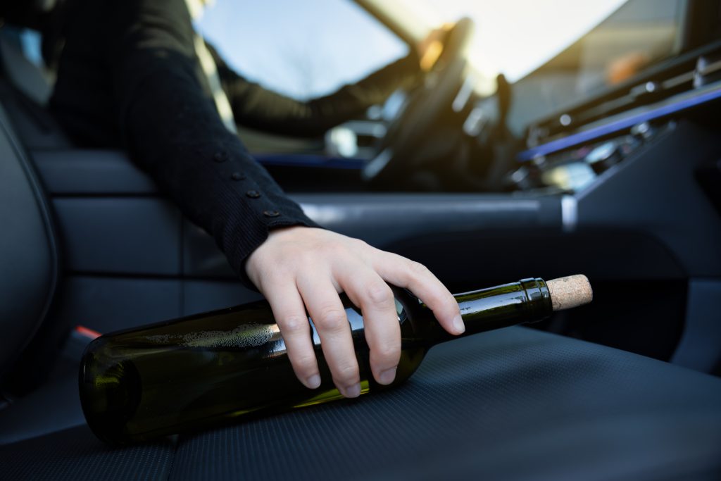 Close-up of a woman's hand holding a bottle of alcohol resting in the passenger's seat